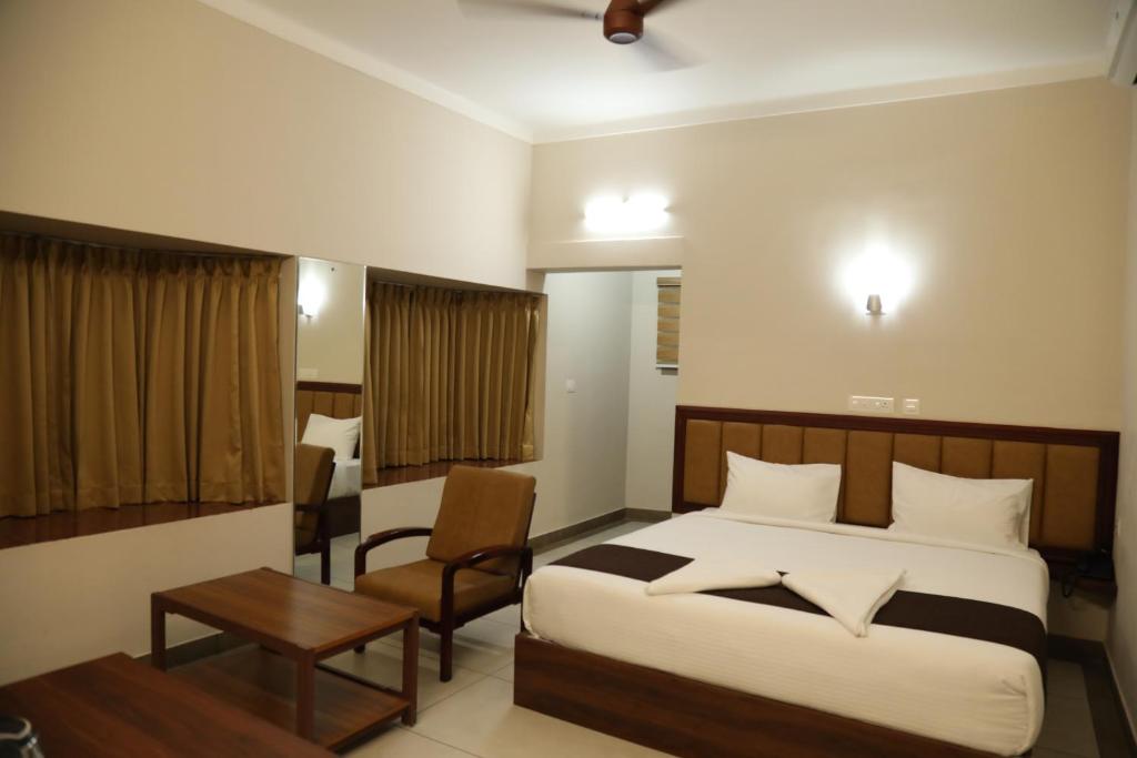 a bedroom with a bed and a chair and a table at Kalathil Kshetra Inn in Guruvāyūr