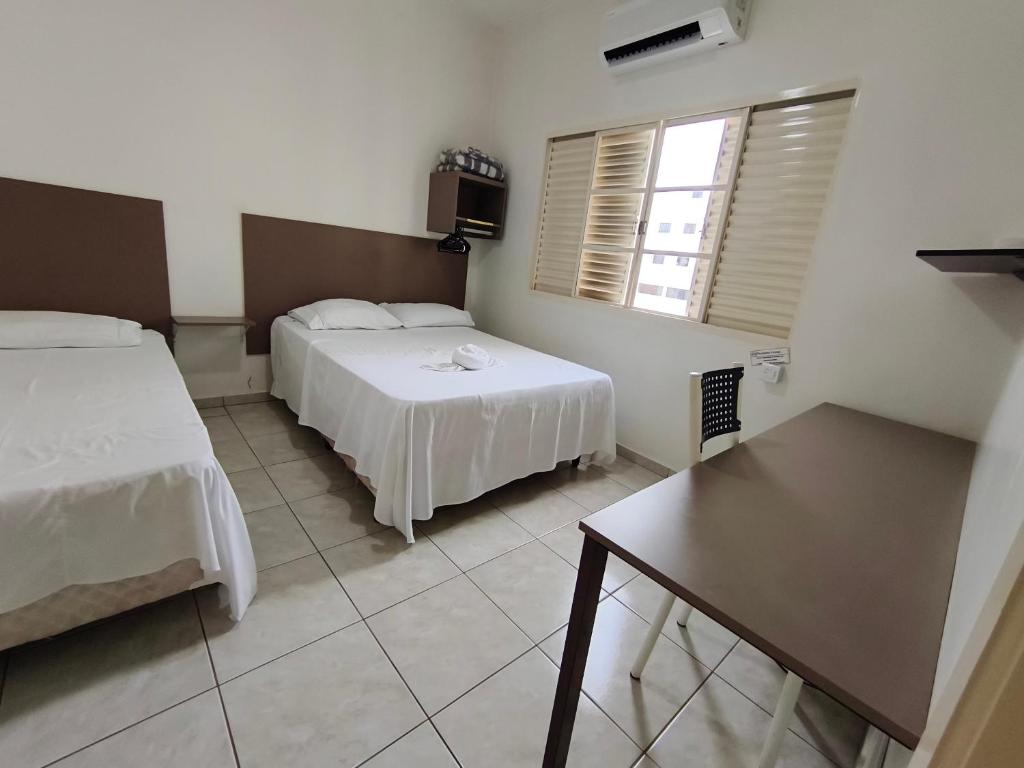 a bedroom with two beds and a table in it at Hotel Mirian in Patos de Minas