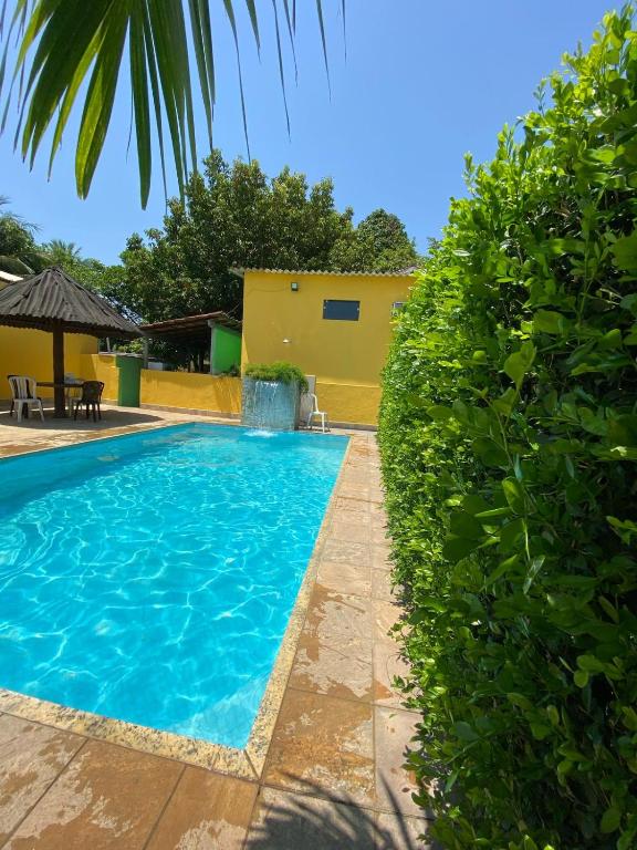 a swimming pool next to a yellow building and some bushes at Pousada do pc in Bom Jesus do Itabapoana