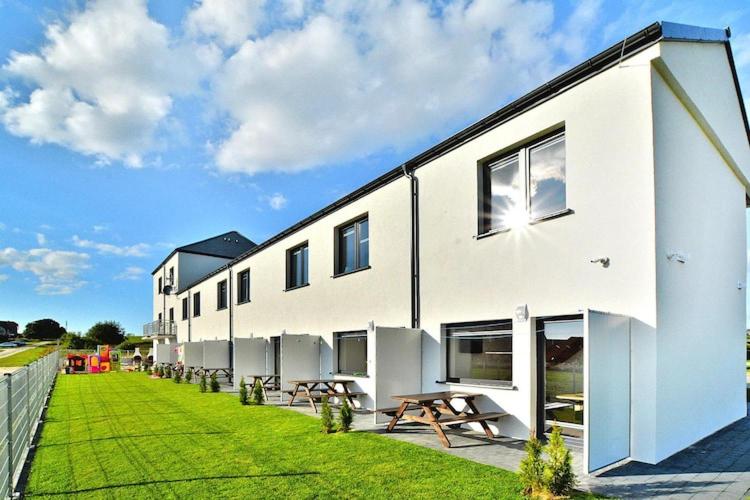 a white building with benches next to a grass field at Comfortable holiday homes with a summer pool in Jarosławiec