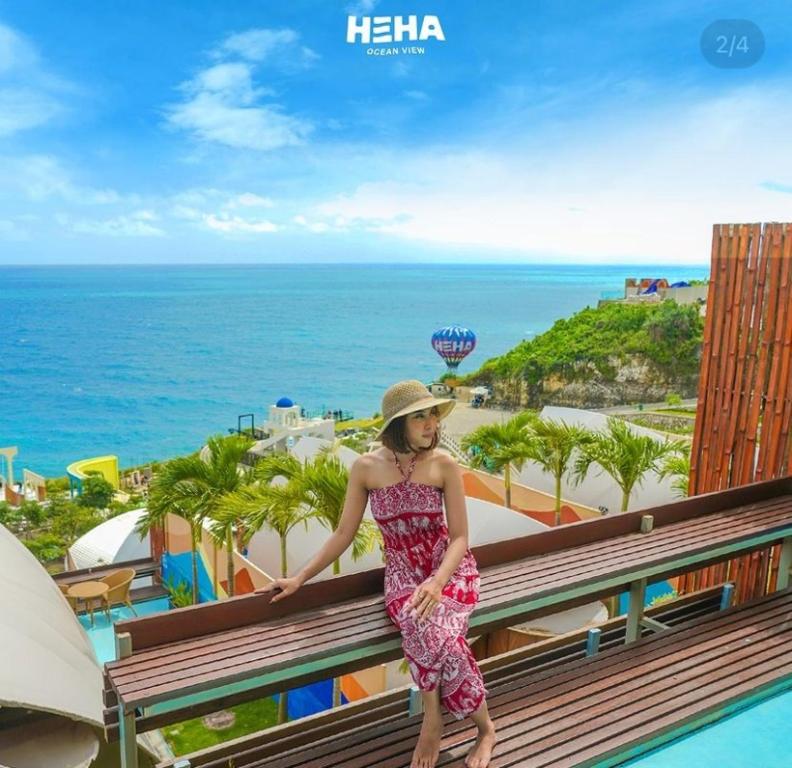 a woman in a dress and hat standing on a balcony overlooking the ocean at HeHa Ocean Glamping dan Cabin in Ngundel