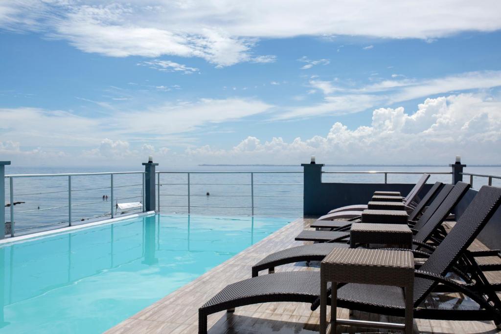 a deck with chairs and a swimming pool with the ocean at Palmbeach Resort & Spa Mactan, Cebu in Mactan