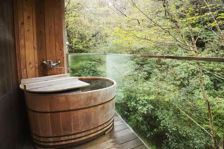 a wooden tub on a deck with a view of a forest at Condominium Sakura in Hakone