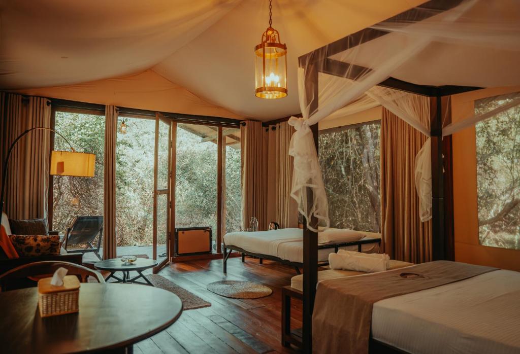 a bedroom with two beds and a table and windows at Chena Wilds Wilpattu in Horuwila
