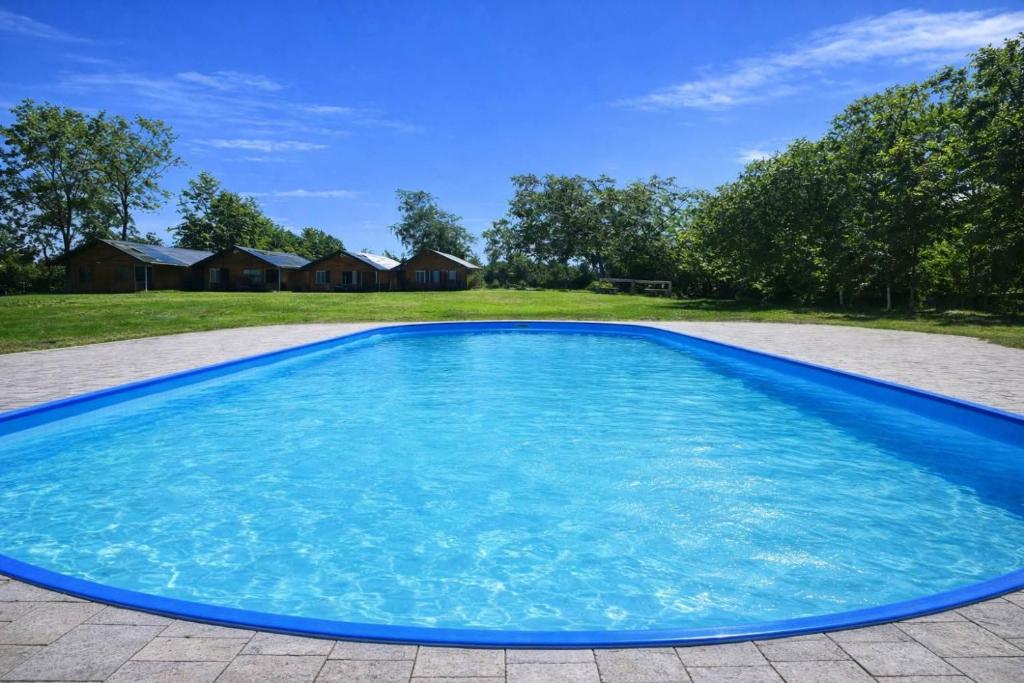 a large blue swimming pool with a house in the background at By The Way - domki nad morzem in Paprotno
