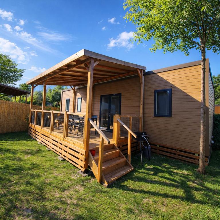 a cabin with a porch and a wooden deck at Le Cocon Mobil Home à 150 m de la plage Camping 5 Etoiles Les Dunes Parc Aquatique in Torreilles
