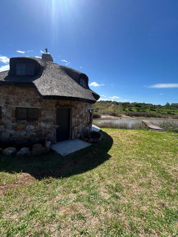 an old stone building with a thatched roof on a field at DaisyRiver Cottage in Port Alfred