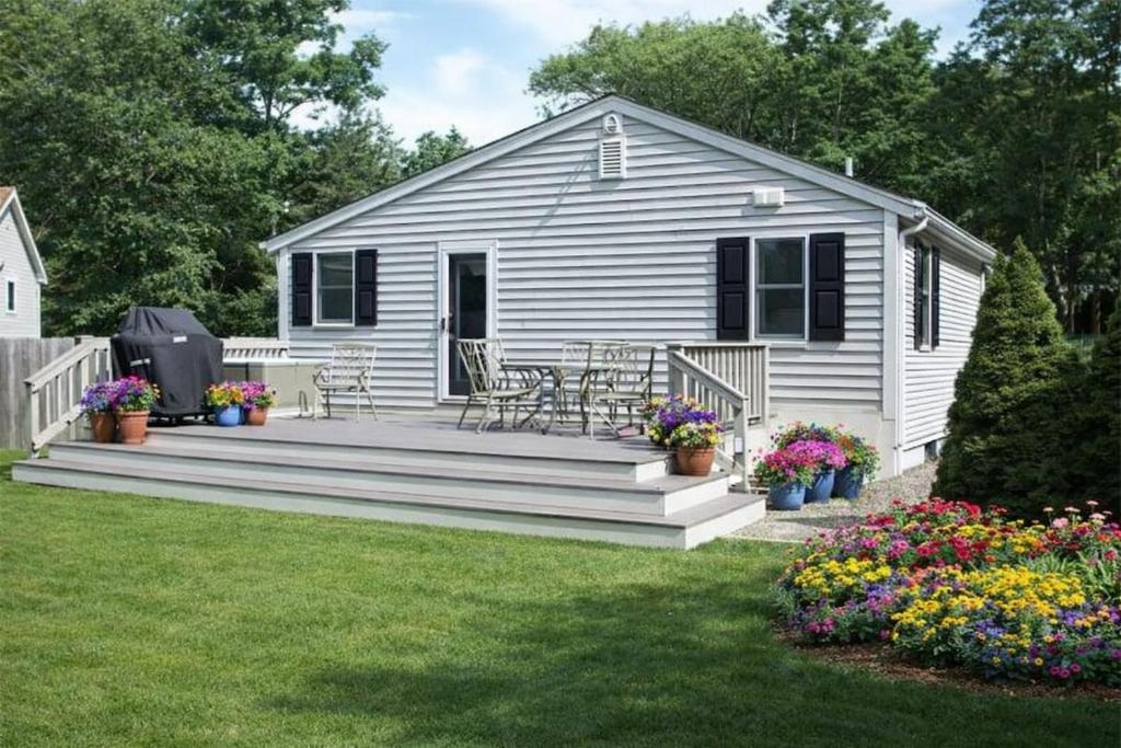 a white house with a deck with chairs and flowers at Cape Lake Private Beach Fire Table in Plymouth