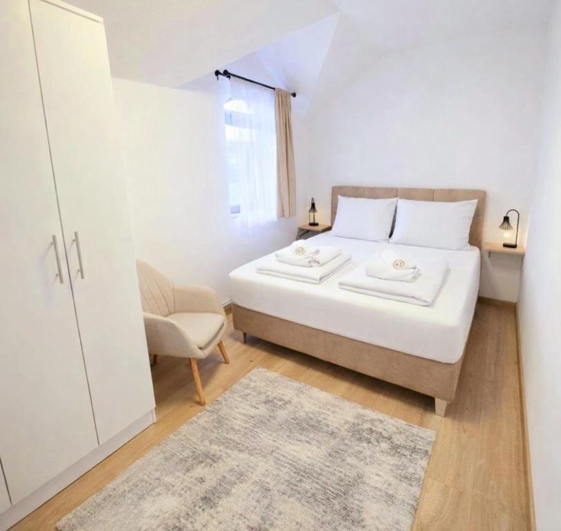 a white bedroom with a bed and a chair at Stan na dan Bumbar in Kostajnica
