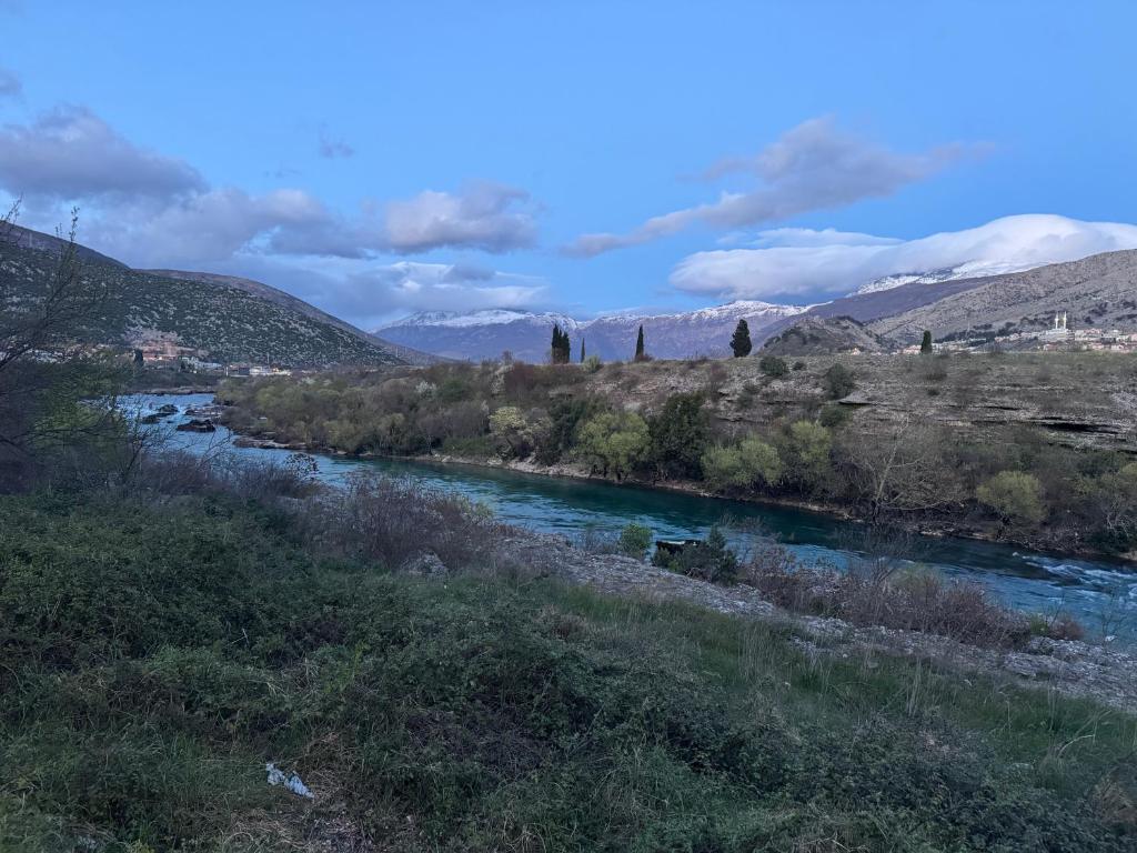 a river in a field with mountains in the background at Neretva Paradise Mostar in Mostar