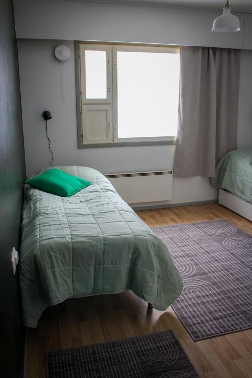 a bedroom with a bed with a green comforter and a window at Hostelli Havumaja in Puumala