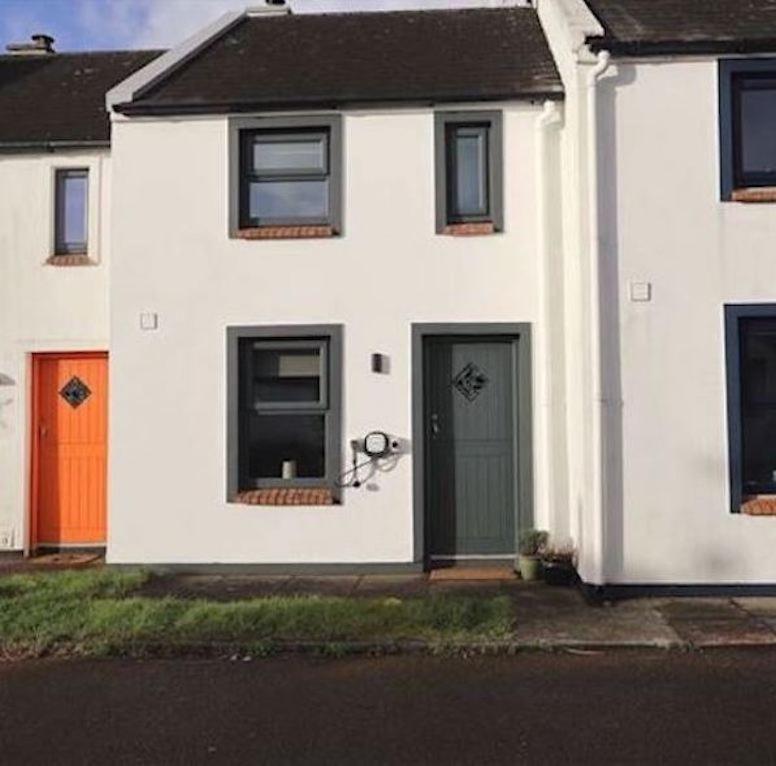a white house with colorful doors on a street at Thrush Cottage in Schull