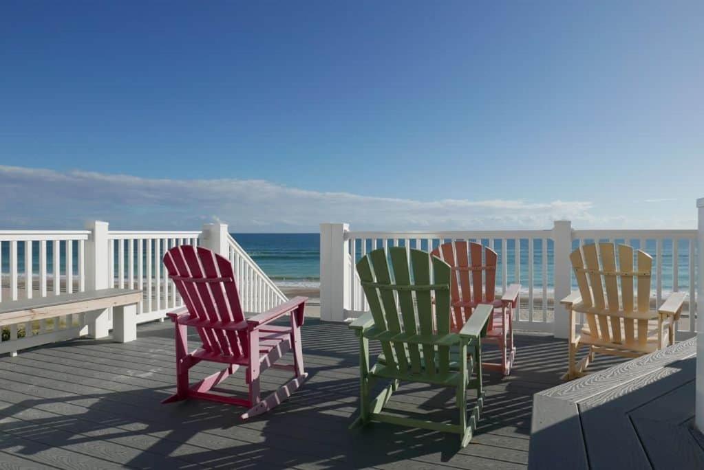 four rocking chairs sitting on a deck overlooking the ocean at Tranquility By The Sea-Oceanside Condo in Salter Path
