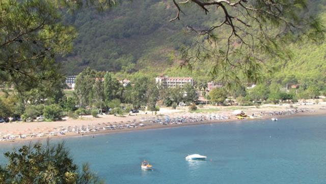 un cuerpo de agua con una playa y un barco en Palmira Hotel, en Adrasan