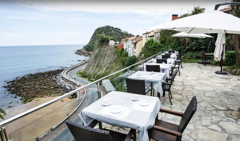 een restaurant met tafels en stoelen en de oceaan bij Hotel Itxas Gain Getaria in Getaria