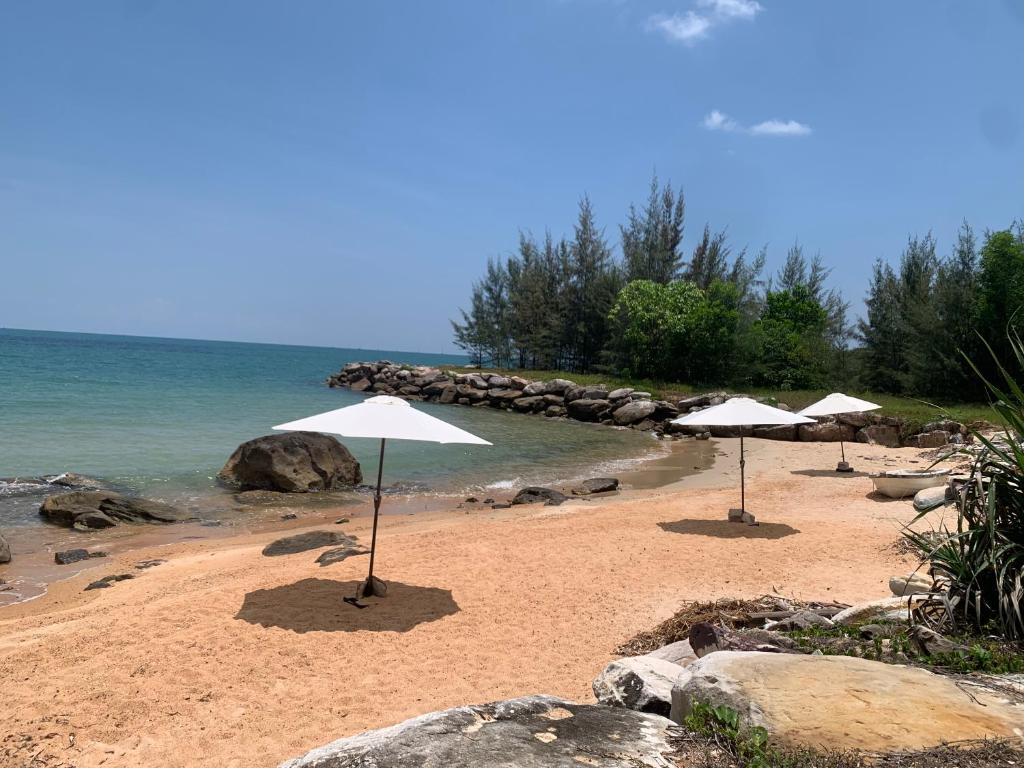 two white umbrellas on a sandy beach with the ocean at An Yen Resort in Phú Quốc