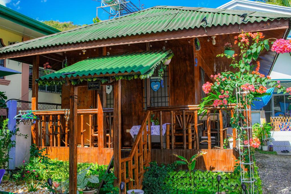 a small house with a green roof and flowers at Puerto Galera Transient Kubo Guest Place in Puerto Galera