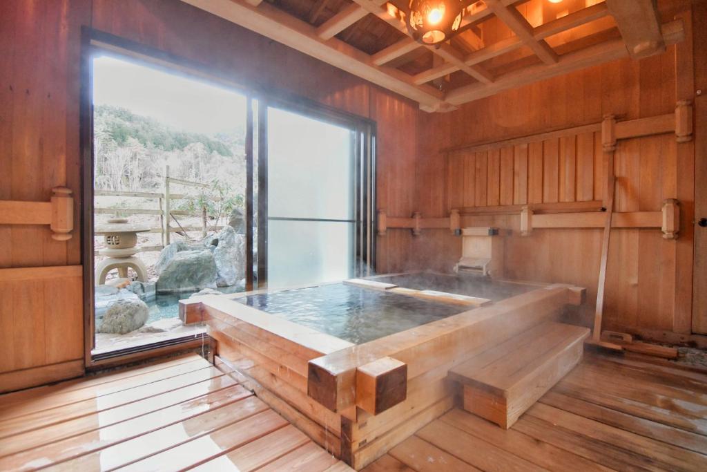 a large bath tub in a room with a large window at 24時間源泉かけ流しを ひとりじめできる 一棟貸しVilla安曇野 in Azumino