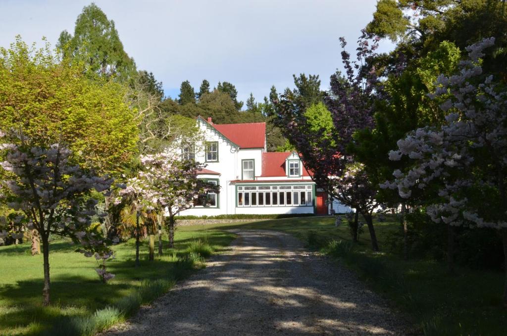 a white house with a red roof and trees at Ashcott Homestead Bed & Breakfast in Takapau