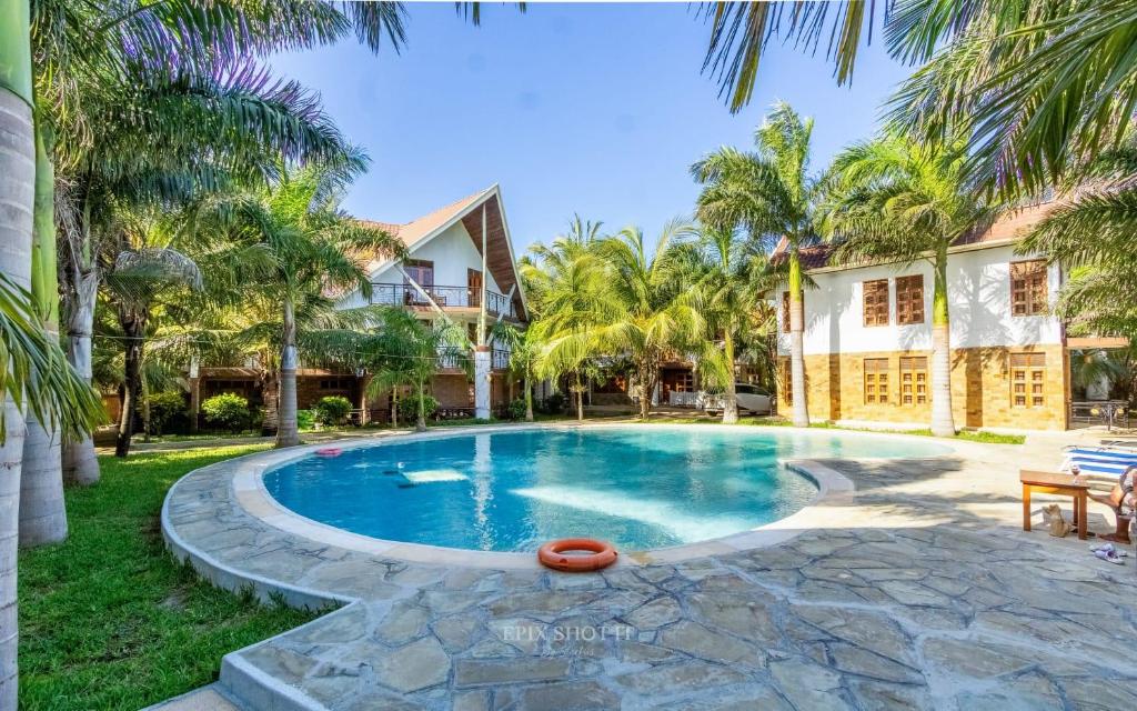 a swimming pool in front of a house with palm trees at Savannah Bstan Luxury Apartment in Diani Beach
