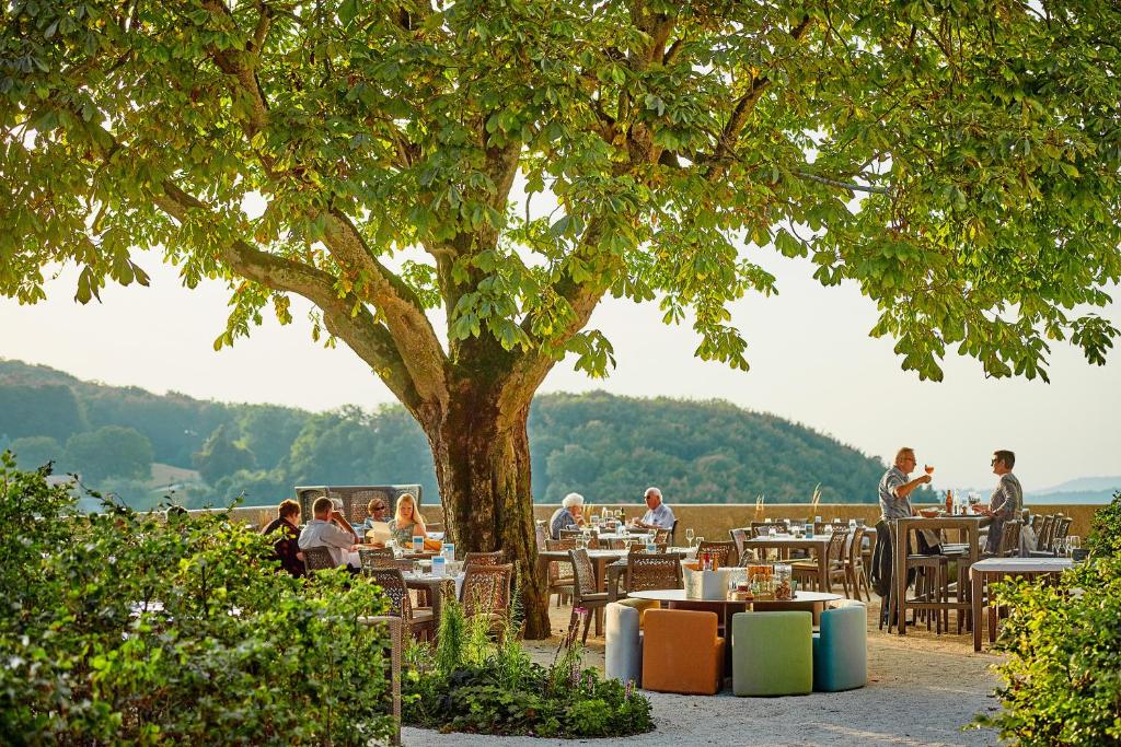 a group of people sitting at tables under a tree at Hotel Bad Ramsach in Läufelfingen