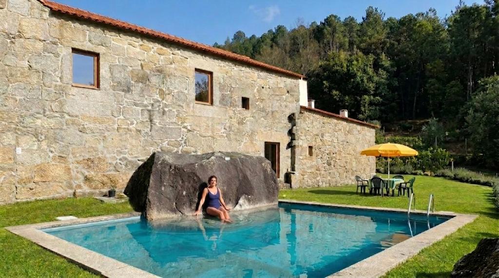 a woman sitting in a rock in a swimming pool at Quinta de Pindela - Natureza e Tradicao in Vila Nova de Famalicão