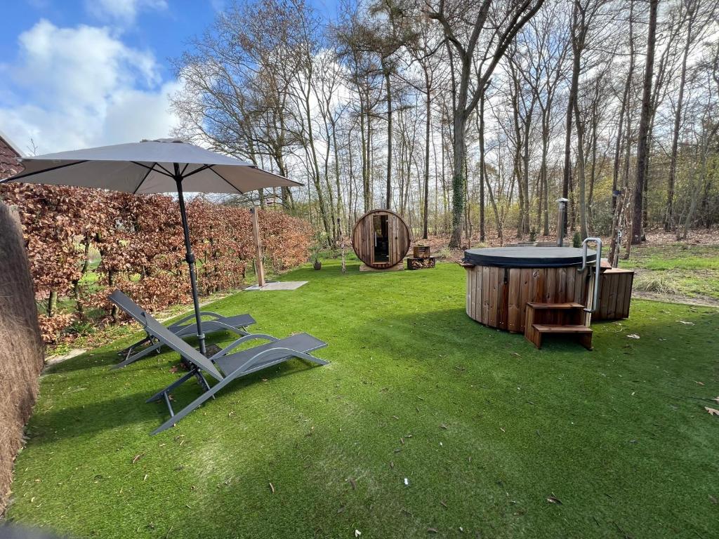 an umbrella and two chairs and a tub in a yard at Wellness in de NATUUR in Neede