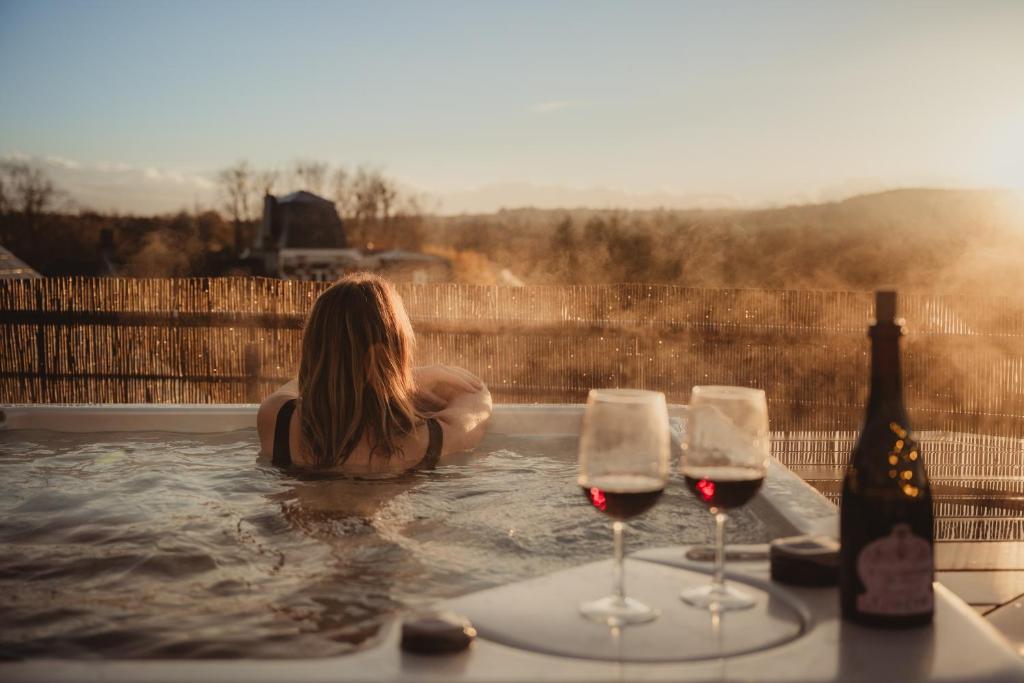 a woman in a hot tub with two glasses of wine at Les Doms d'Alfred - GRINDOM in Plombières