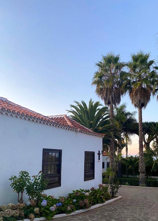 a white house with palm trees in the background at La Vereda - Rural getaway, pool, golf & hiking lovers in Tacoronte