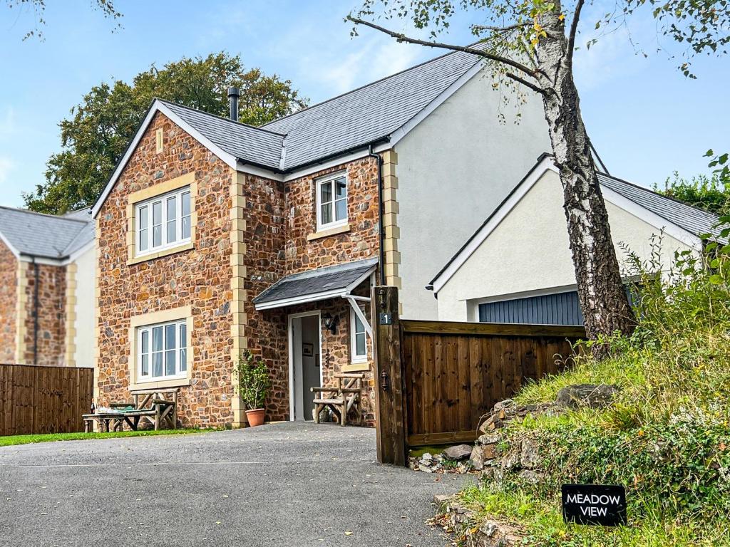 a brick house with a wooden fence in front of it at Meadow View Brushford in Dulverton