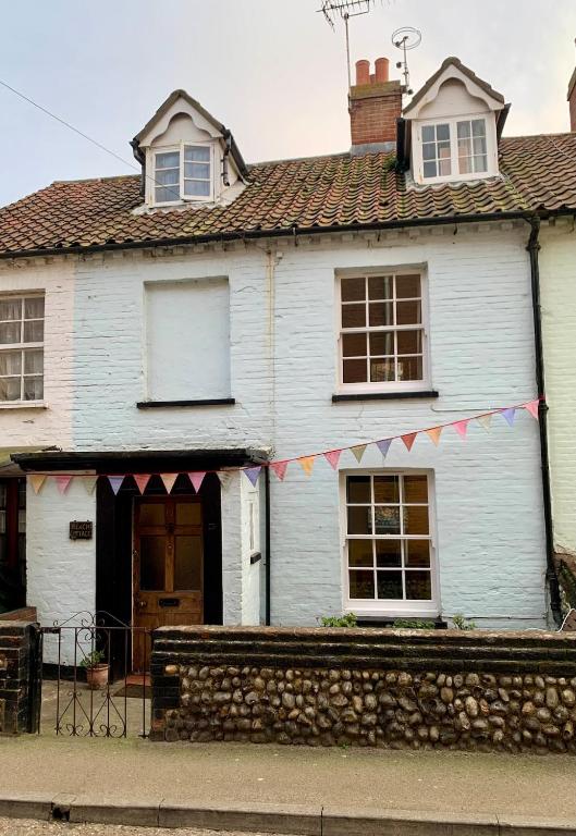 a white house with a string of flags on it at Charming Cottage and Beach Hut in Cromer
