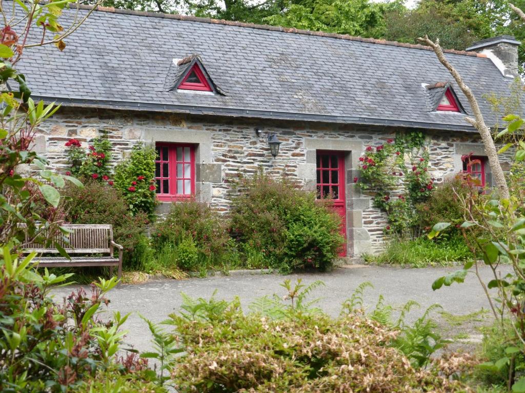 a stone house with red windows and a bench at Moulin De Beuzidou in Saint-Urbain