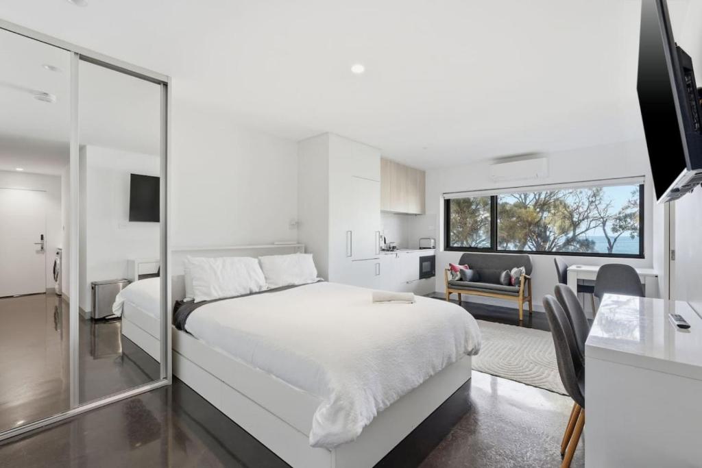 a white bedroom with a large bed and a kitchen at Modern Beachside Studio in Kingston Beach