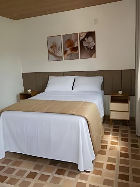 a bedroom with a white bed and two pictures on the wall at Chalés do Lago Lumiar in Nova Friburgo