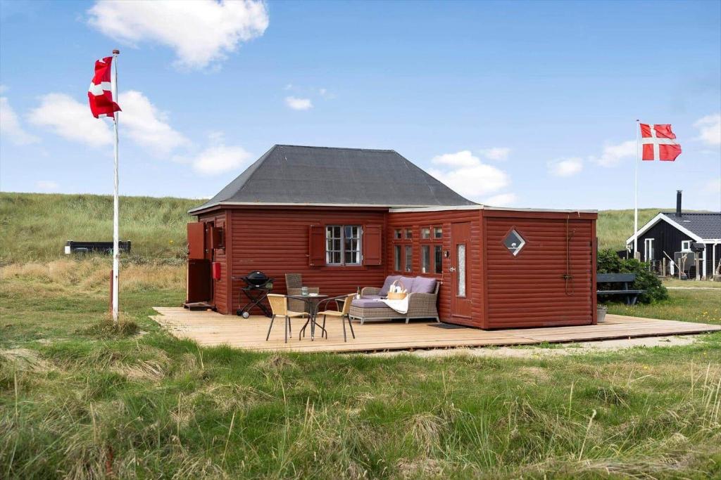 a red cabin with a deck in a field at 1355-Vestervig-Klitvej-4 in Agger