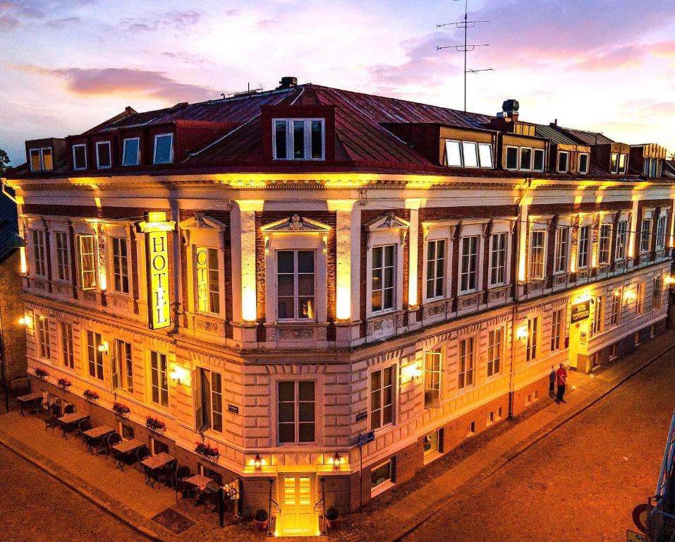 Oświetlony wieczorem narożny budynek hotelu z klasyczną elewacją i dużym neonowym szyldem.