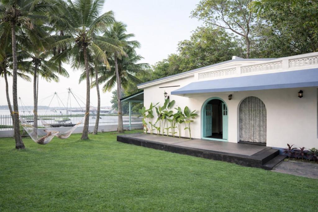 a white house with a porch and palm trees at Kumarakom Homes in Kumarakom