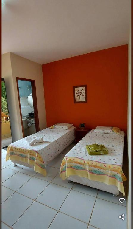 two beds in a room with an orange wall at Pousada Elshadai in Uruçuca