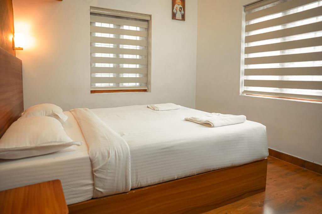 a white bed in a room with two windows at Cloud 9 Homestay, Thekkady in Thekkady