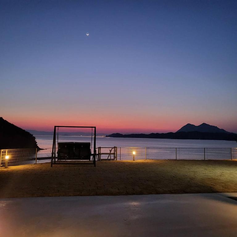 a bench on the beach with the sunset in the background at ヴィラ倉橋 in Kure