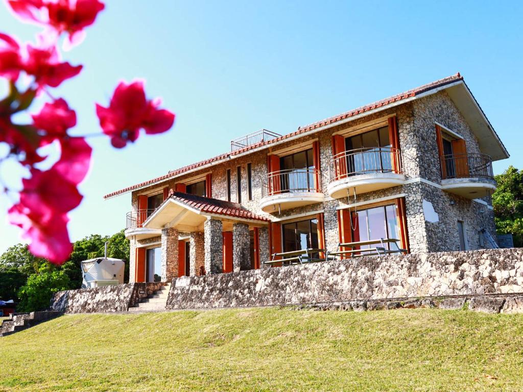 a large house on a hill with red flowers at Garden BBQ and Stay ANCHOR in Miyakojima
