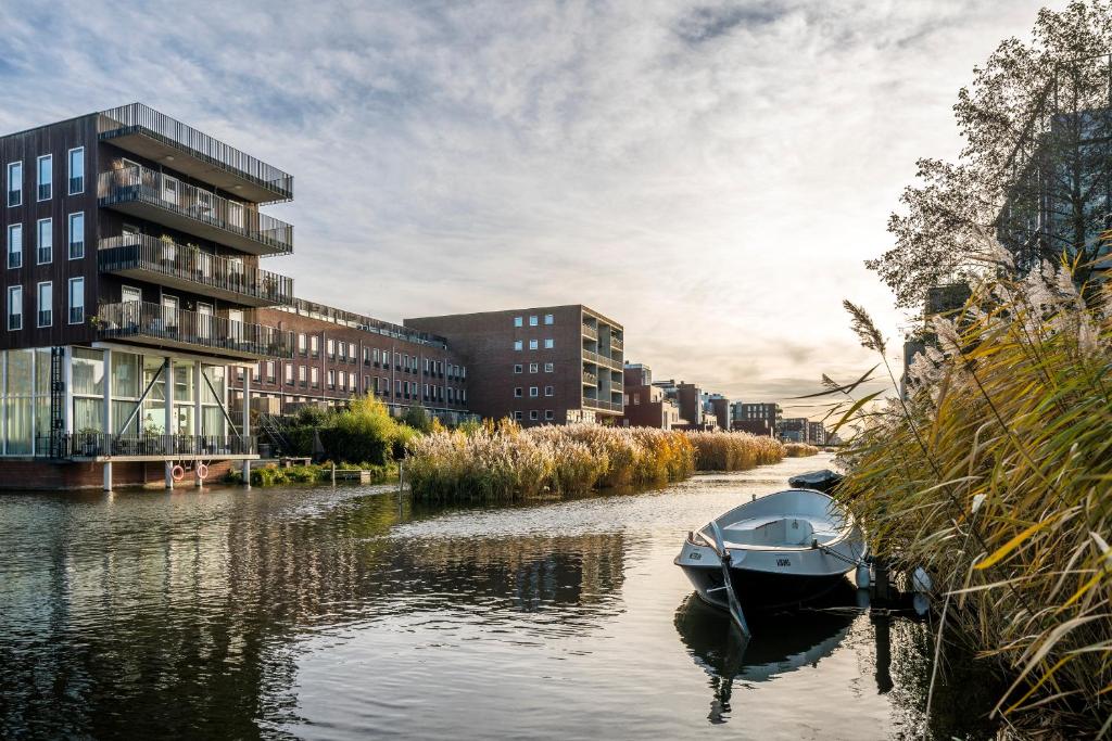 una barca è ormeggiata in un fiume con edifici di Rieteiland B&B ad Amsterdam