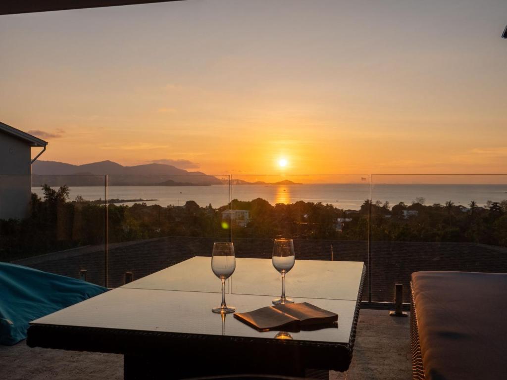 two wine glasses on a table with a view of the sunset at Luxe 4BR Sunset Seaview Villa Private Infinity in Plai Laem