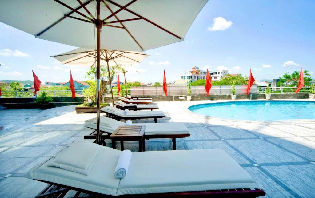 a group of lounge chairs and an umbrella by a pool at Mondial Hotel Hue in Hue