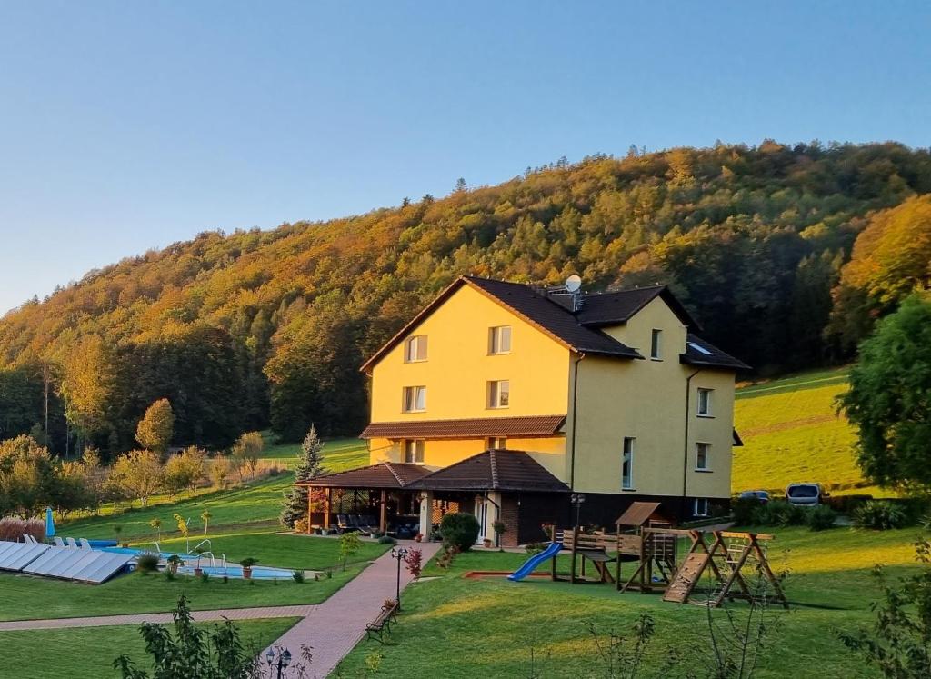 a large yellow house with a playground on a hill at Agroturystyka Willa Maria in Bystrzyca Kłodzka