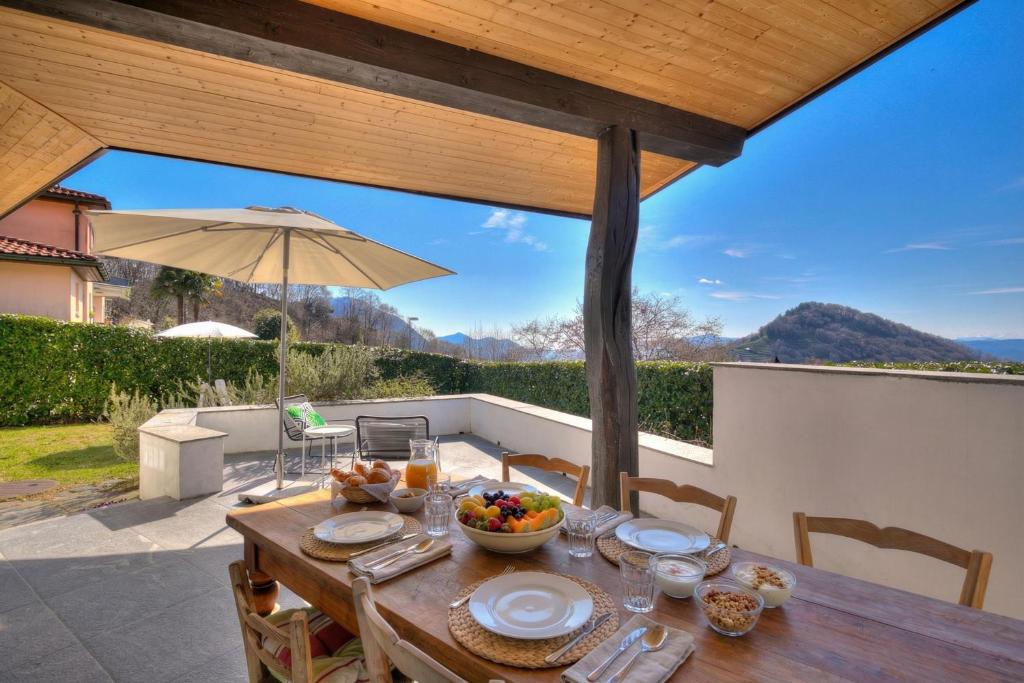 a wooden table with a bowl of fruit and an umbrella at La Cà Da Brè - Garden House with Views - Happy Rentals in Lugano