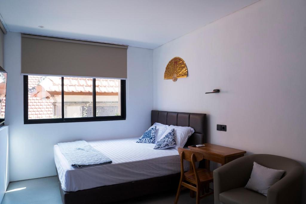 a bedroom with a bed and a chair and a window at Hakon Canggu Boutique Hostel in Canggu