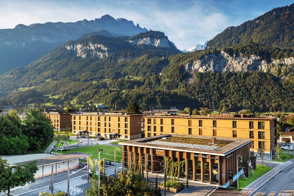 a large yellow building with mountains in the background at SWISSPEAK Resorts by Pierre & Vacances Premium Meiringen in Meiringen