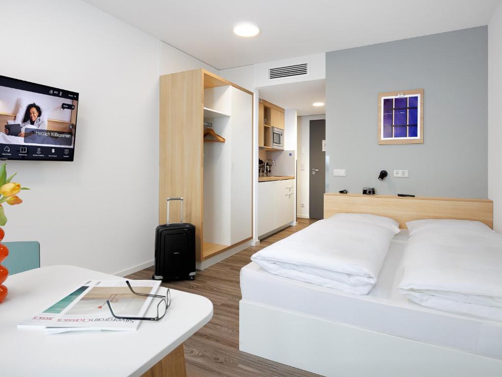 a white bedroom with a white bed and a table at smartments Frankfurt Airport in Frankfurt