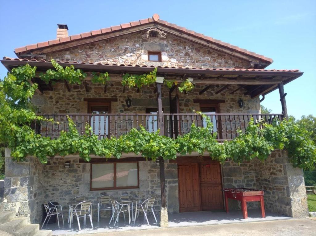 a stone house with a balcony and tables and chairs at Apartamentos La Barcenilla in Herada